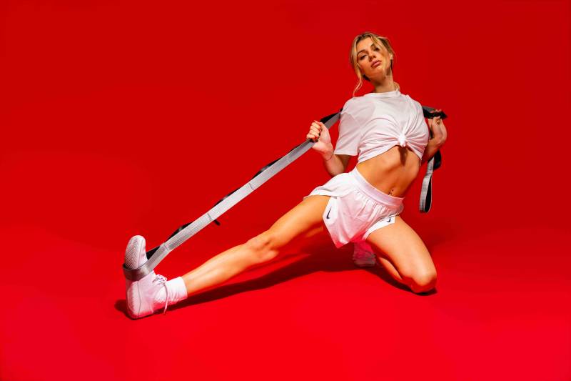 Rose Physical Therapy patient in white athletic wear demonstrating a shoulder mobility stretch using the Brazyn strap’s independent loops to safely increase her range of motion.