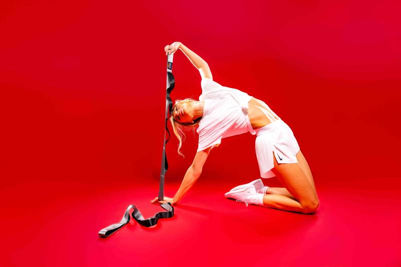 Female athlete in white CrossFit gear at Rose Physical Therapy using the 12-loop Brazyn strap around her foot to perform a controlled leg stretch for improved athletic alignment.
