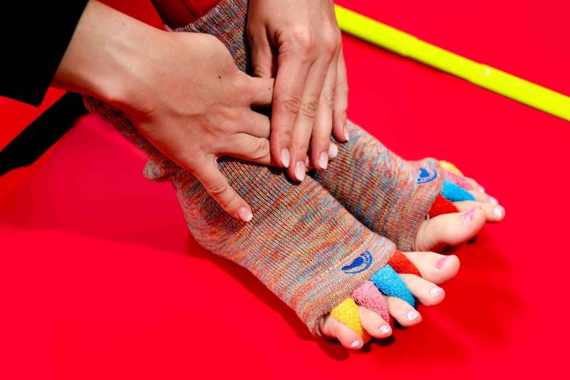 Close-up of feet wearing red crew socks with four built-in toe separators, a common tool recommended by D.C. physical therapists to help fix overlapping toes and bunions.