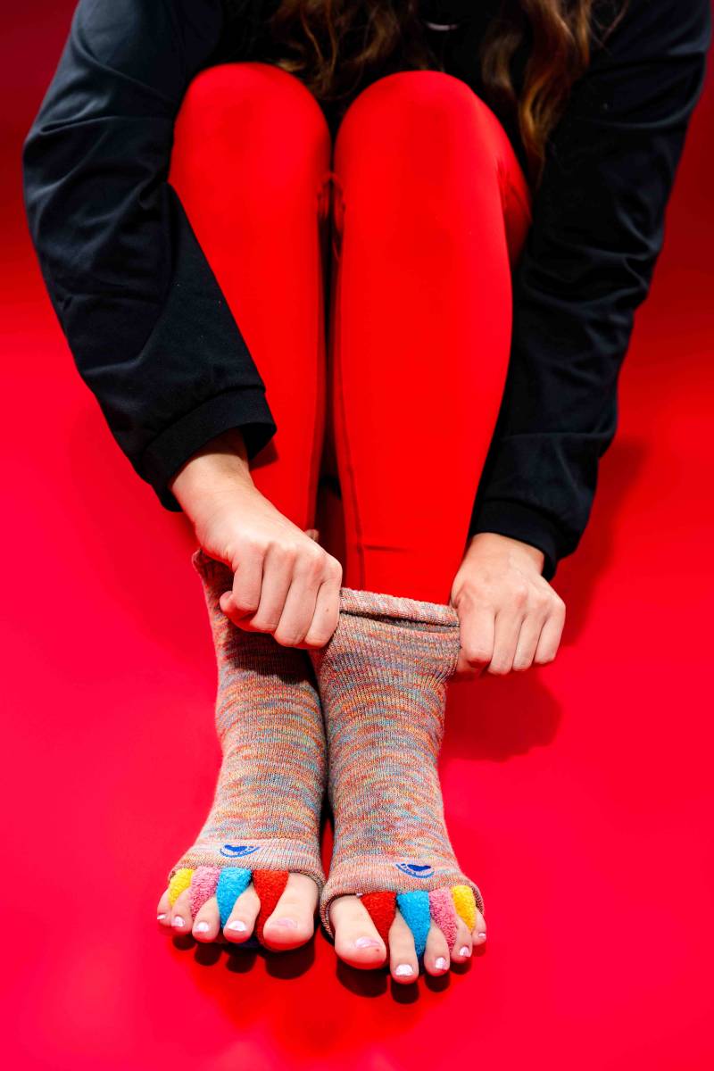 A person wearing red 'The Original Foot Alignment Socks' which feature toe spacers to gently stretch and realign feet, often used as at-home care following a physical therapy session in D.C.