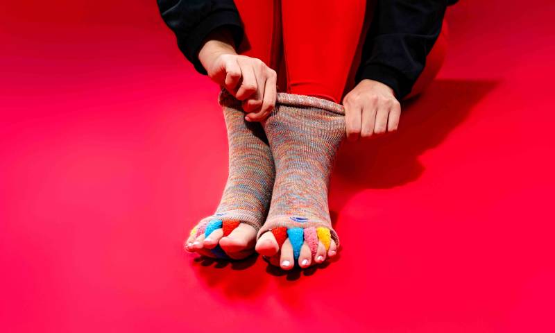 Close-up of red crew-style foot alignment socks with four integrated toe separators, used by Washington, D.C. physical therapists to improve foot mechanics and toe splay for patients.Blog or Service Page) "Red Original Foot Alignment Socks featured at Rose Physical Therapy; a professional-grade alternative to silicone spacers that uses fabric dividers to gently realign toes and alleviate plantar fasciitis and
